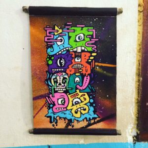 “A small piece on canvas painted in vibrant colours which says "que Honda" but each letter is a cartoon monster of my creation.”